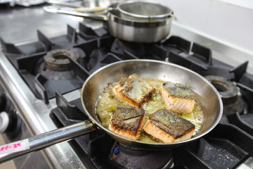 The chef is frying salmon in the pan in the kitchen.