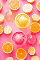 Orange and lemon juice maker, fresh summer juice, cut lemon and orange fruit with red and yellow juice container and squeezer,top view, on a pink board with strong backlight