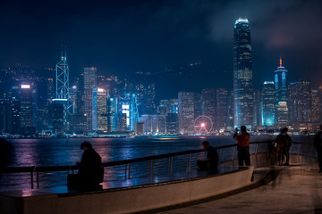 Hong Kong cityscape at night. Tourists walking on the waterfront