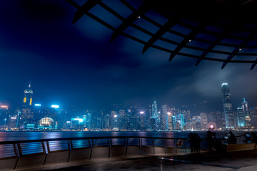 Hong Kong cityscape at night. Tourists walking on the waterfront