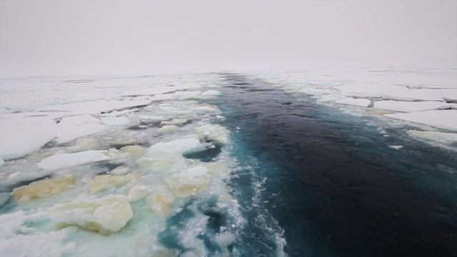 The view from the aft of an icebreaker vessel cruising in the frozen ocean with chunks of sea ice floating