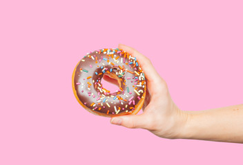Female hand holding colorful donut on pastel pink background