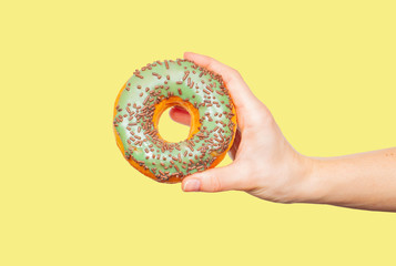 Female hand holding colorful donut on pastel yellow background