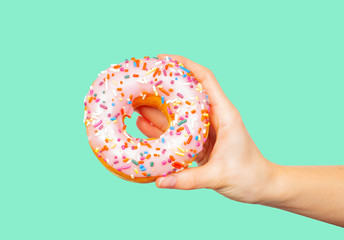 Female hand holding colorful donut on pastel green background