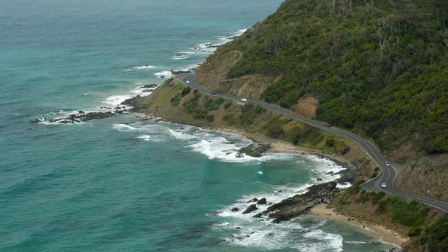 Looking down on the winding Great Ocean Road at Lorne's Teddy's lookout, Australia. Coastal views and ocean waves crashing into the eroded shore as cars weave along the iconic highway. PAN UP SHOT