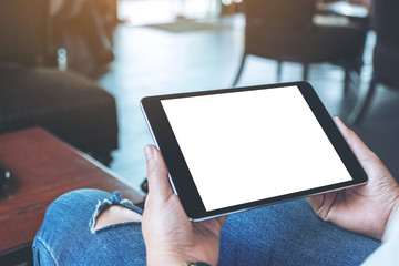 Mockup image of a woman sitting and holding black tablet pc with blank white desktop screen horizontally in cafe