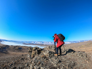 Fototapeta premium camera man in bright orange winter jacket takes landscape photo of Baikal lake in Russia