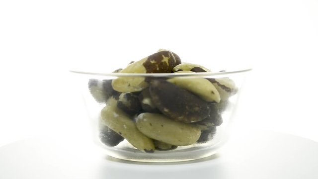 Transparent glass bowl with Brazil nuts rotating on a white background. Flat plane. Eye level