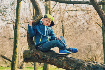 The boy sits on a tree during a spring walk . Child's play