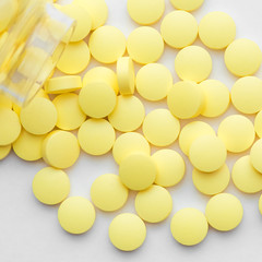 Yellow pills scattered from a glass jar on a white background.