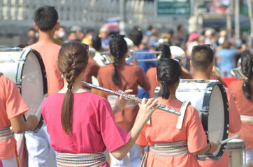 Young girl wear thai traditional suit playing flute for show in marching band paraded on street with blur crowded background, woman flute player in marching band, flute player in marching band parade © sunghorn