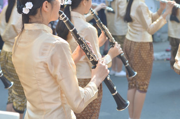 Young girl wear thai traditional suit playing clarinet for show in marching band paraded on street with blur crowded background, marching band clarinet player, clarinet player in marching band parade