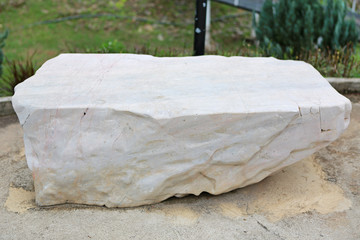 Rock seat on green grass garden. Natural stone chair in park.