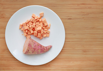 Raw peeled and chopped sweet potatoes in white plate on wood board background with copy space.