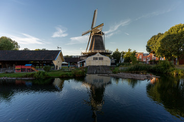 Woodworking windmill in a neighbourhood in Utrecht, The Netherlands, mirrored in the water in the canal in front of it on a bright sunny day with blue sky.