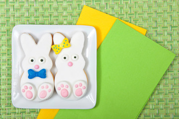 Easter Bunny Sugar Cookies on a plate with green place mat background. Marshmallow fondant covered cookie with candy feet, eyes and nose and tail and bows. Boy and girl. Green and yellow napkins.