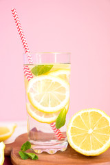 glass of homemade lemonade with lemons, mint and green paper straw on wooden rustic background. Summer refreshing beverage.