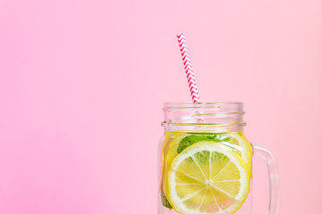 Mason jar glass of homemade lemonade with lemons, mint and red paper straw on pink background. Summer refreshing beverage.
