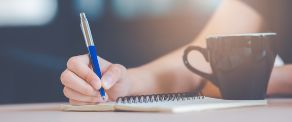 Woman hand is writing on a notepad with a pen.