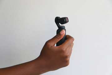 An isolated black African hand holding and filming with a DJI Osmo pocket camera in front of a white surface