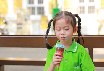 Happy little Asian kid girl enjoy eating ice cream cone with stained around her mouth.