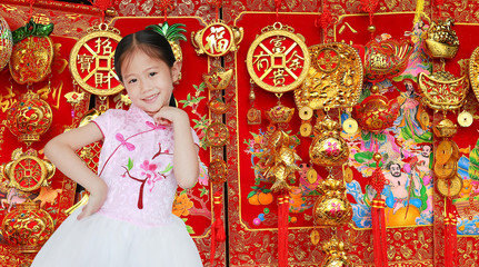 Smiling little Asian child girl wearing pink Traditional Chinese dress for Chinese New Year celebration on good luck item background.