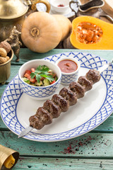 kofta kebab on skewer with fresh vegetables and ketchup on blue wooden table
