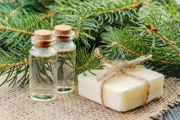 Two bottles of spruce essential oil, natural soap and fir branches on linen napkin. The concept of alternative medicine.