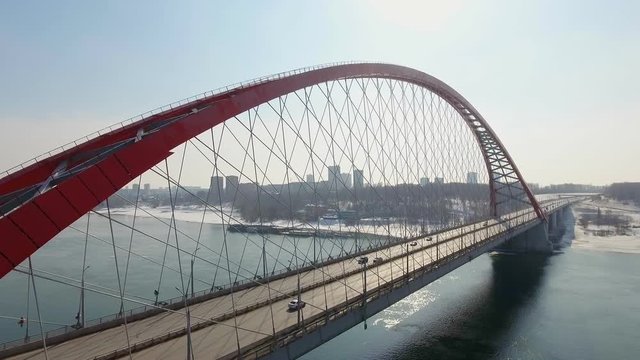 Helicopter shot beside suspension red brigde with medium traffic cars driving across the road. industrial concept, sunny shining day. City landscape with fog and scyscrappers behind. drone shot 4k