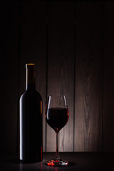 Bottle and glass of red wine on wooden background