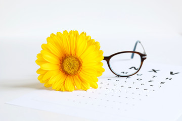 Occhiali da vista, fiore giallo, pezzuola e foglio stampato tabella optometrica su uno sfondo bianco