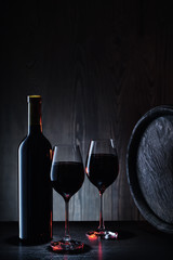 Red wine in glass and bottle on background of wooden barrels and walls
