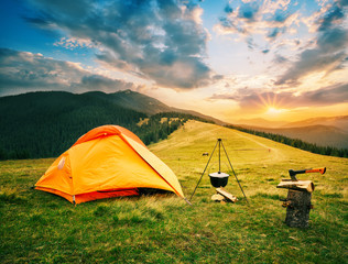 Camp touristique dans les montagnes avec tente et chaudron sur le feu au coucher du soleil