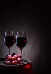 Two glasses of red wine and bunch of grapes on barrel