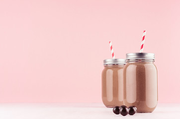 Exquisite light milk chocolate dessert in jars with chocolate balls, red straw, silver cap on modern elegant pink color background.