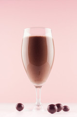 Chocolate milkshake in elegance glass with chocolate candies on white wooden table and pastel light pink wall, vertical.