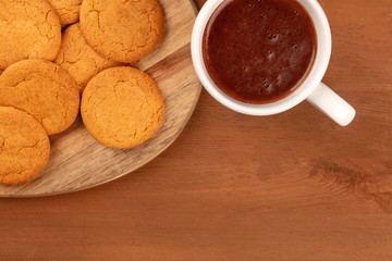 A closeup of ginger cookies, shot from the top with a cup of hot chocolate on a dark rustic wooden background with a place for text