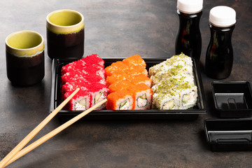 Sushi rolls and sashimi in a black plastic box. Traditional Japanese cuisine with salmon, fish, wasabi, soy sauce, and ginger.