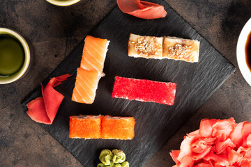 Sushi rolls and sashimi in a black stone plate. Traditional Japanese cuisine with salmon, fish, wasabi, soy sauce, and ginger. Chopsticks and two cups of traditional sake
