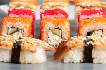 Sushi rolls and sashimi in a black stone plate. Traditional Japanese cuisine with salmon, fish, wasabi, soy sauce, and ginger. Chopsticks and two cups of traditional sake