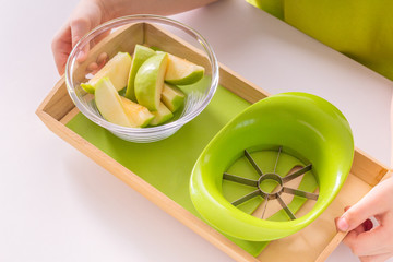 Children's hands hold a wooden tray with montessori materials for a lesson from the practical life zone. Apple slicer, cutting board,green apple. Isolate on white background.