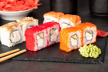 Sushi rolls and sashimi in a black stone plate. Traditional Japanese cuisine with salmon, fish, wasabi, soy sauce, and ginger. Chopsticks and two cups of traditional sake