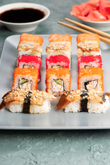 Sushi rolls and sashimi in a grey plate. Traditional Japanese cuisine with salmon, fish, wasabi, soy sauce, and ginger. Chopsticks and two cups of traditional sake