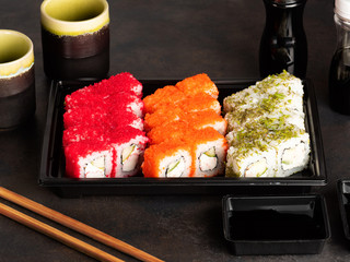 Sushi rolls and sashimi in a black stone plate. Traditional Japanese cuisine with salmon, fish, wasabi, soy sauce, and ginger. Chopsticks and two cups of traditional sake