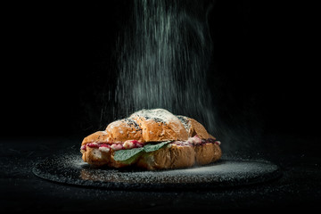 Fresh baked croissants with falling powdered sugar on dark background