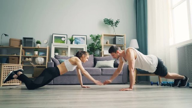 Happy young couple girl and guy are doing advanced pushups and clapping hands in apartment smiling and enjoying working out together. People and sports concept.