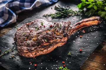 Zelfklevend Fotobehang Freshly grilled tomahawk steak on slate plate with salt pepper rosemary and parsley herbs © weyo