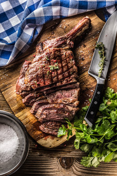 Freshly grilled tomahawk steak on slate plate with salt pepper rosemary and parsley herbs. Sliced pieces of juicy beef steak