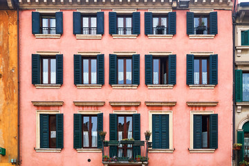 The ancient facade of the building with a balcony and a lot of windows. Flowers on the balcony.