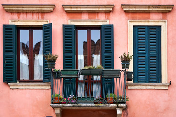 Fototapeta na wymiar Ancient facade of the building. Balcony and two windows. Flowers on the balcony.